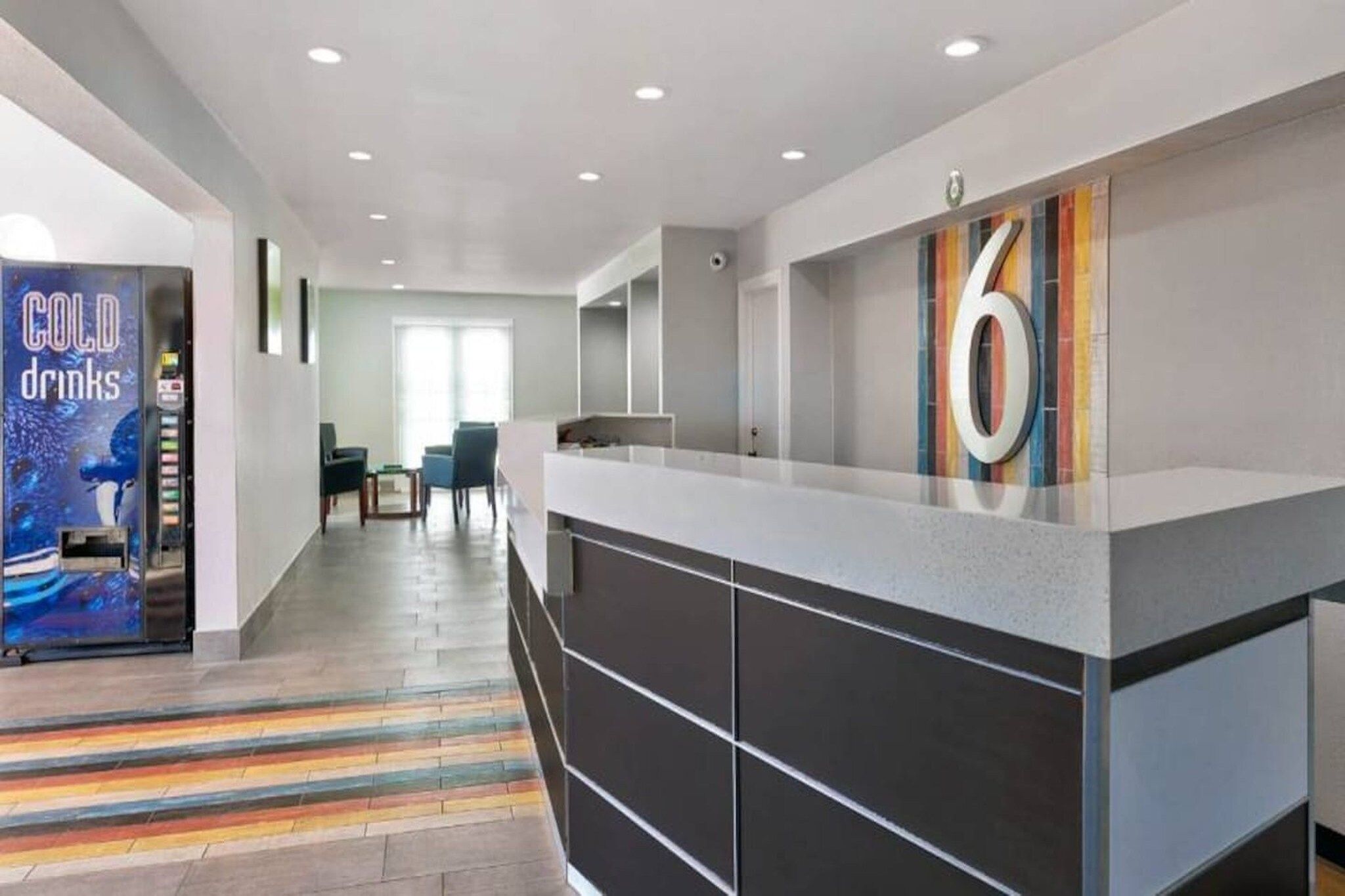A modern hotel lobby with a reception desk, a vending machine, and a colorful striped floor.