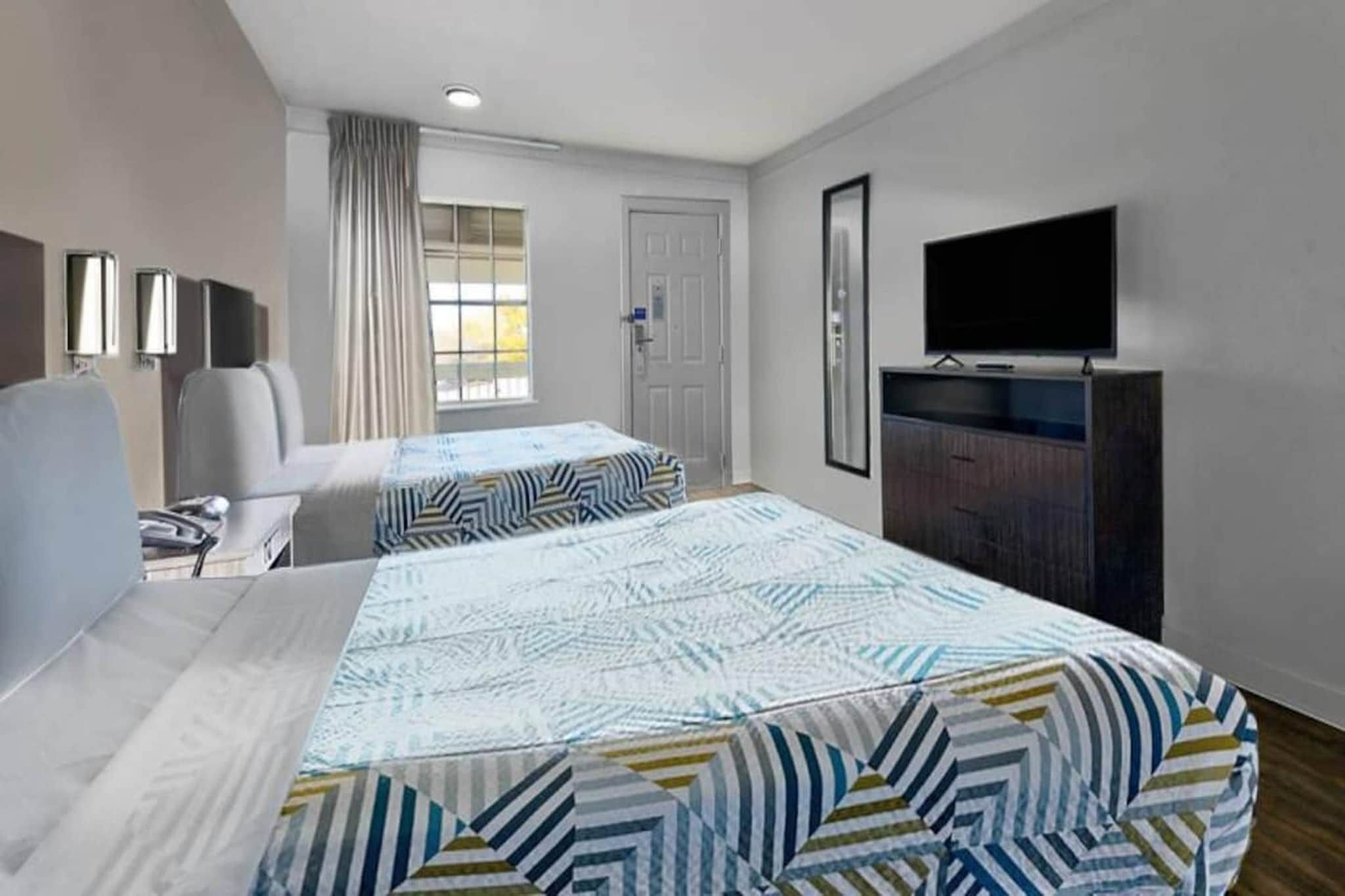 A hotel room with two beds, a TV, a desk, and a chair.