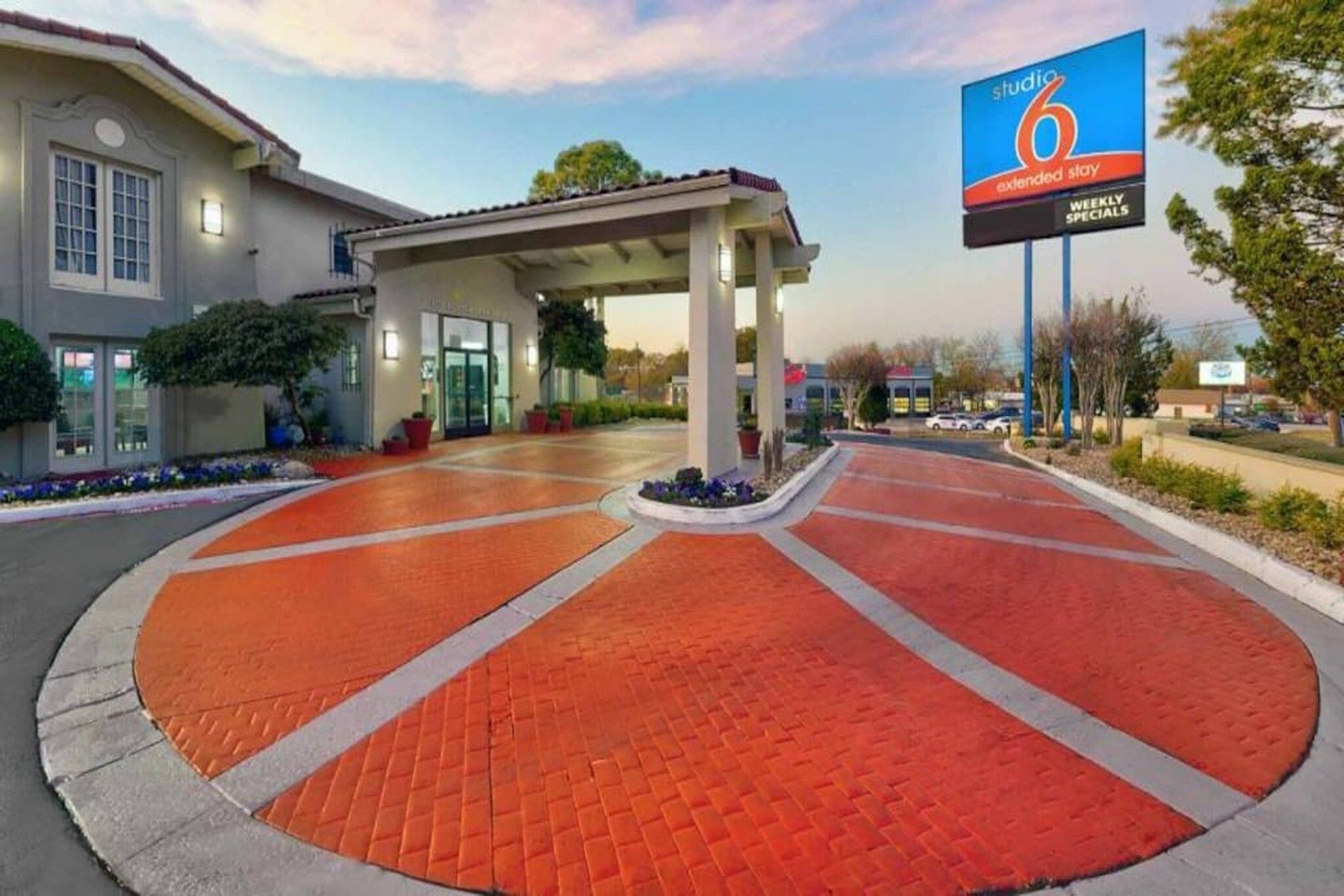 A hotel entrance with a covered walkway, a parking lot, and a billboard advertising weekly specials.