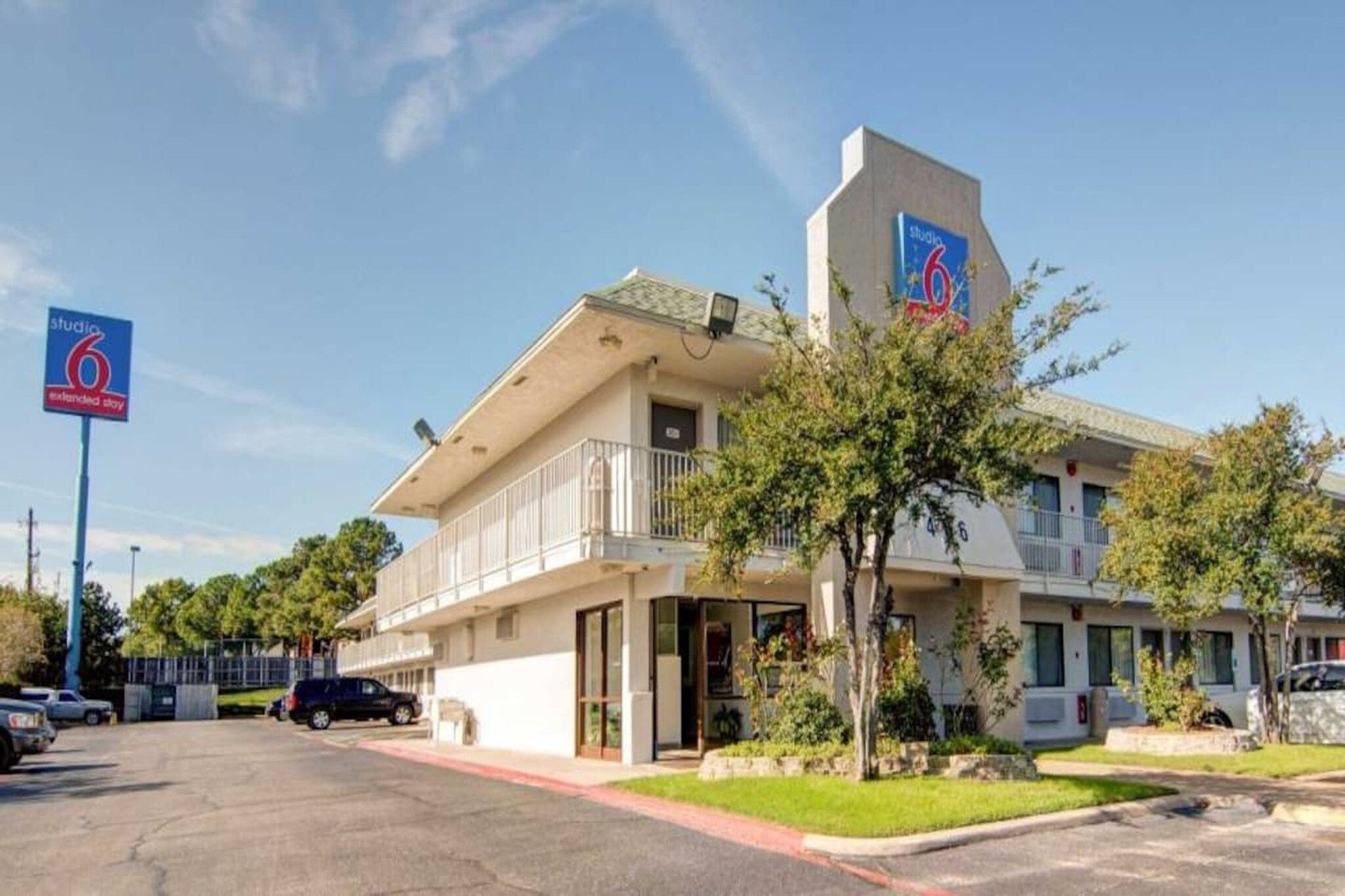 A two-story motel with a balcony on the second floor, a parking lot in front, and a clear sky.