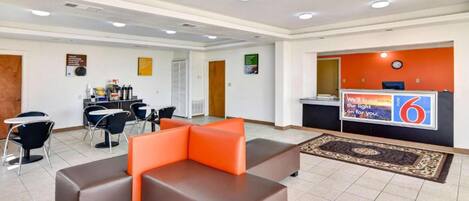 A hotel lobby with a reception desk, seating area, and a small kitchenette.