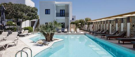 A modern hotel with a swimming pool, lounge chairs, and a clear sky.