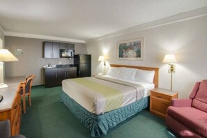 Quarto de hotel com cama, escrivaninha, cadeira, cozinha compacta e um quadro na parede.