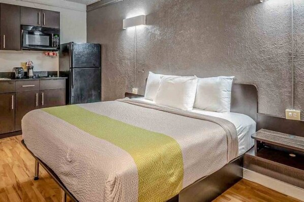 Quarto de hotel com cama, mesa de cabeceira, cômoda, micro-ondas e geladeira.