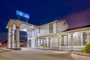 Un motel avec une grande enseigne, plusieurs entrées et un parking couvert.