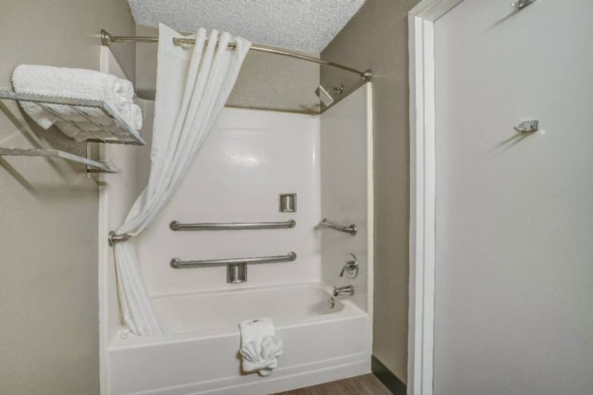 Un baño con bañera, barras de apoyo, cortina de ducha y un perchero.