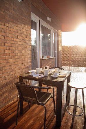 An outdoor patio with a brick wall, a table set with cups and plates, and two chairs. - New Listing (Roma)