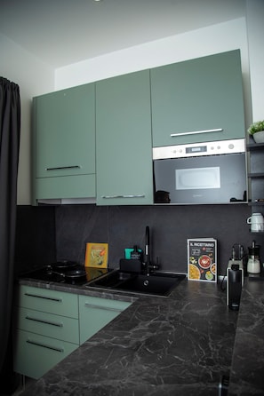 A modern kitchen with teal cabinets, a black countertop, and a built-in oven. - New Listing (Roma)