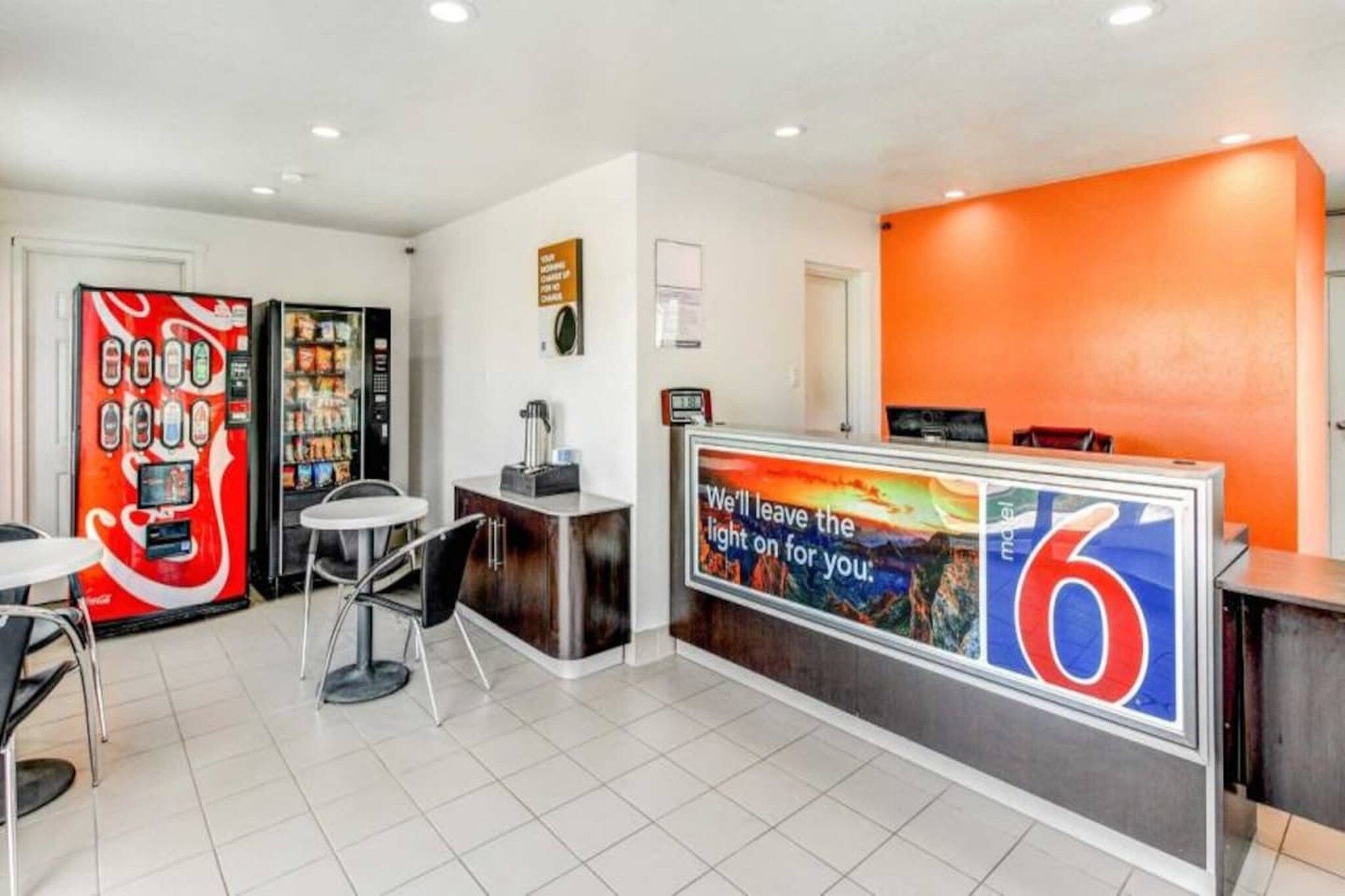 A hotel reception area with a Coca-Cola vending machine, a small table with chairs, and a large sign with the number 6.