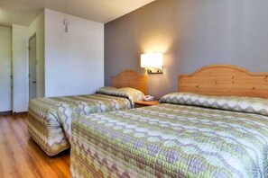 A hotel room with two beds, wooden headboards, a bedside table with a lamp, and a wall clock. - Spacious 2 Full Beds | Non-Smoking (Dallas)