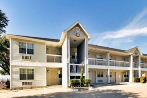 A multi-story motel with a central entrance, balconies, and a parking lot. - Spacious 2 Full Beds | Non-Smoking (Dallas)