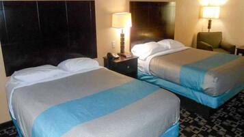 Quarto de hotel com duas camas, uma mesa de cabeceira com abajur e uma cadeira.