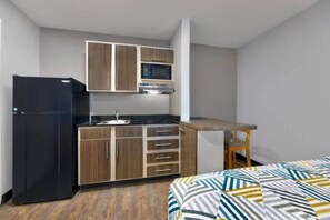 A compact kitchen with a refrigerator, microwave, sink, and wooden cabinets. - 1 Queen Bed | Smoking, Micfridge (North Richland Hills)