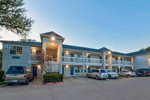 A multi-story motel with a central courtyard, parking lot, and a row of vehicles parked in front. - 1 Queen Bed | Smoking, Micfridge (North Richland Hills)