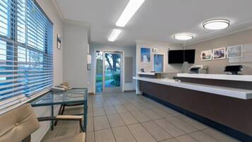 A reception area with a glass partition, a reception desk, a flat-screen TV, and a door leading outside.