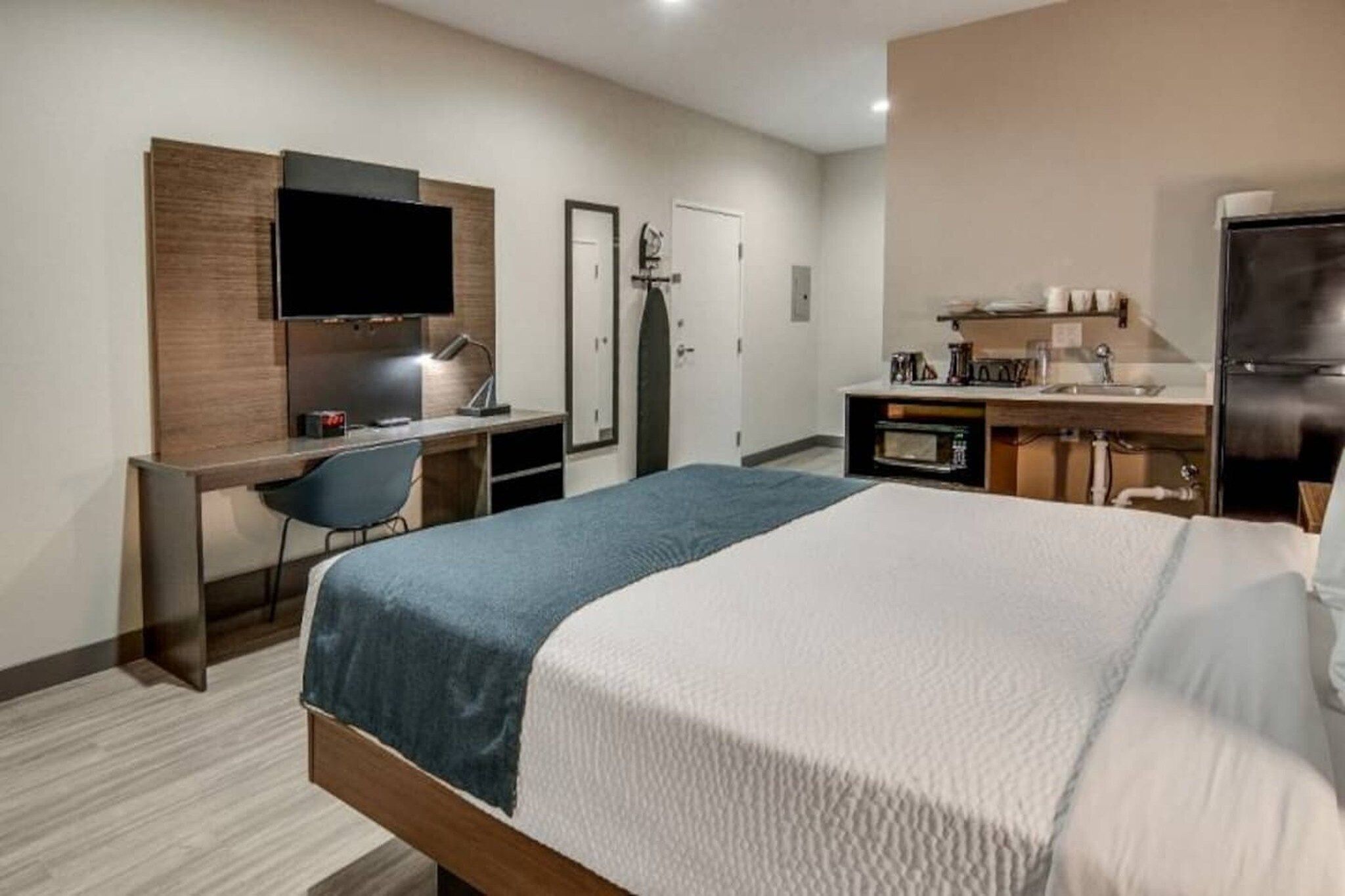 Hotelkamer met een bed, een bureau met stoel, een televisie, een kledingkast, een deur, een kitchenette en een koelkast.