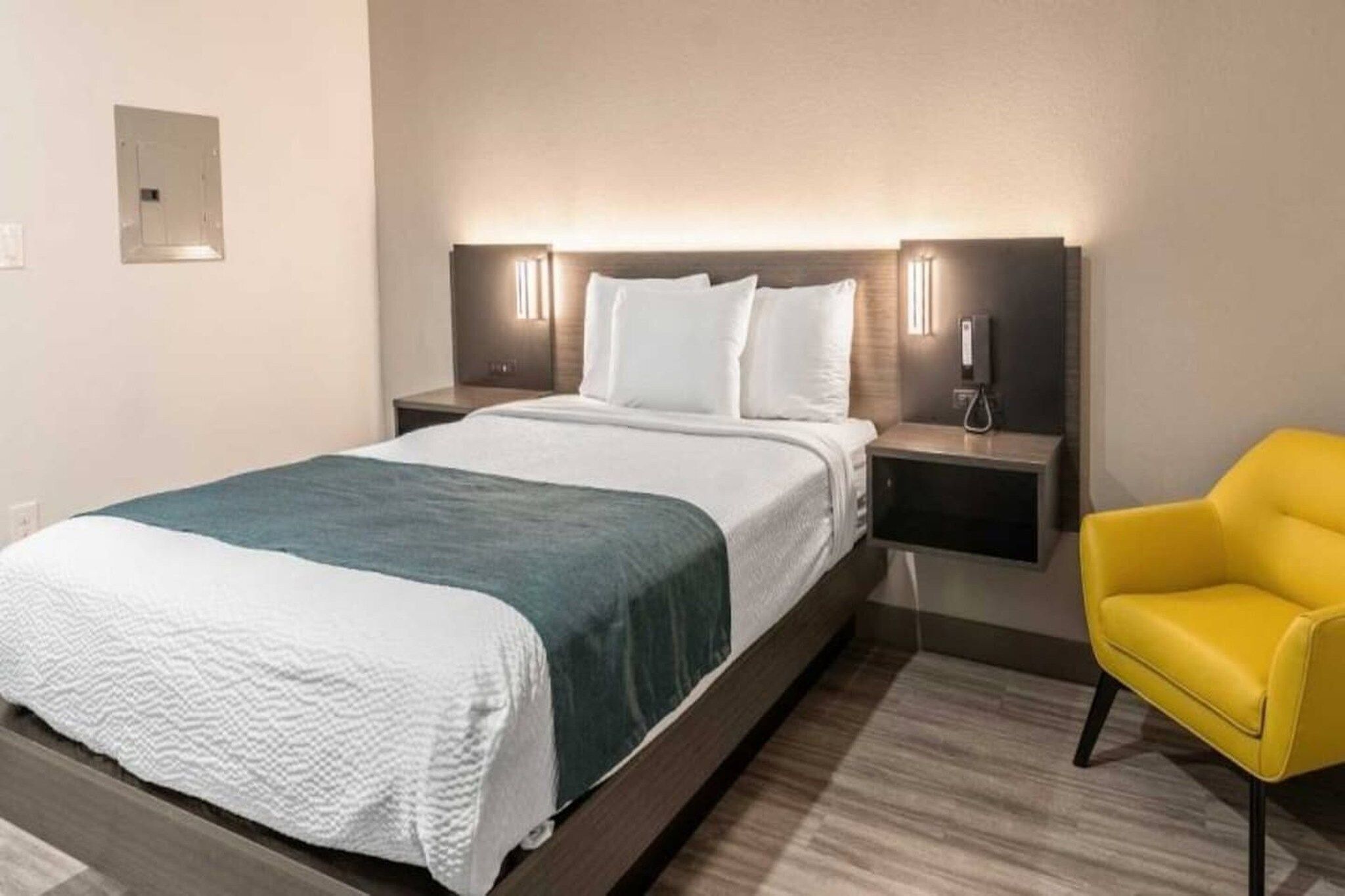 A hotel room with a bed, bedside tables, a chair, and a wall-mounted phone.