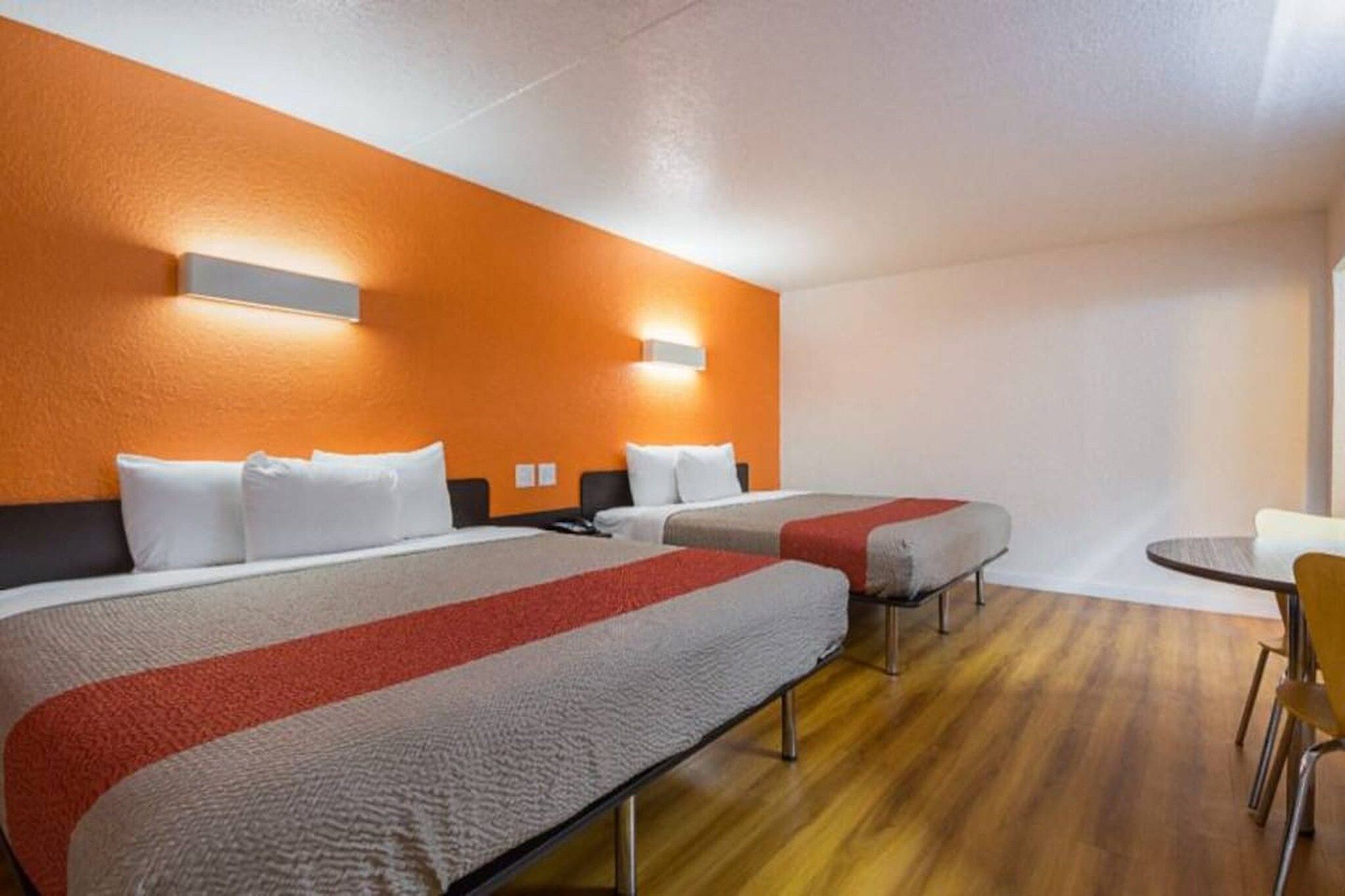 A hotel room with two beds, a small table, and a chair.
