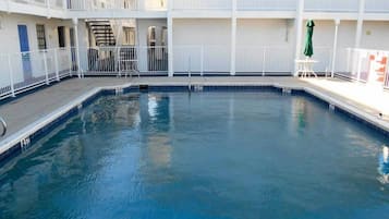 A swimming pool with a white surrounding deck and a multi-level building with balconies.