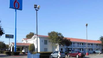 A motel with a red roof, a blue sign with the number 6, and a parking lot with several cars.