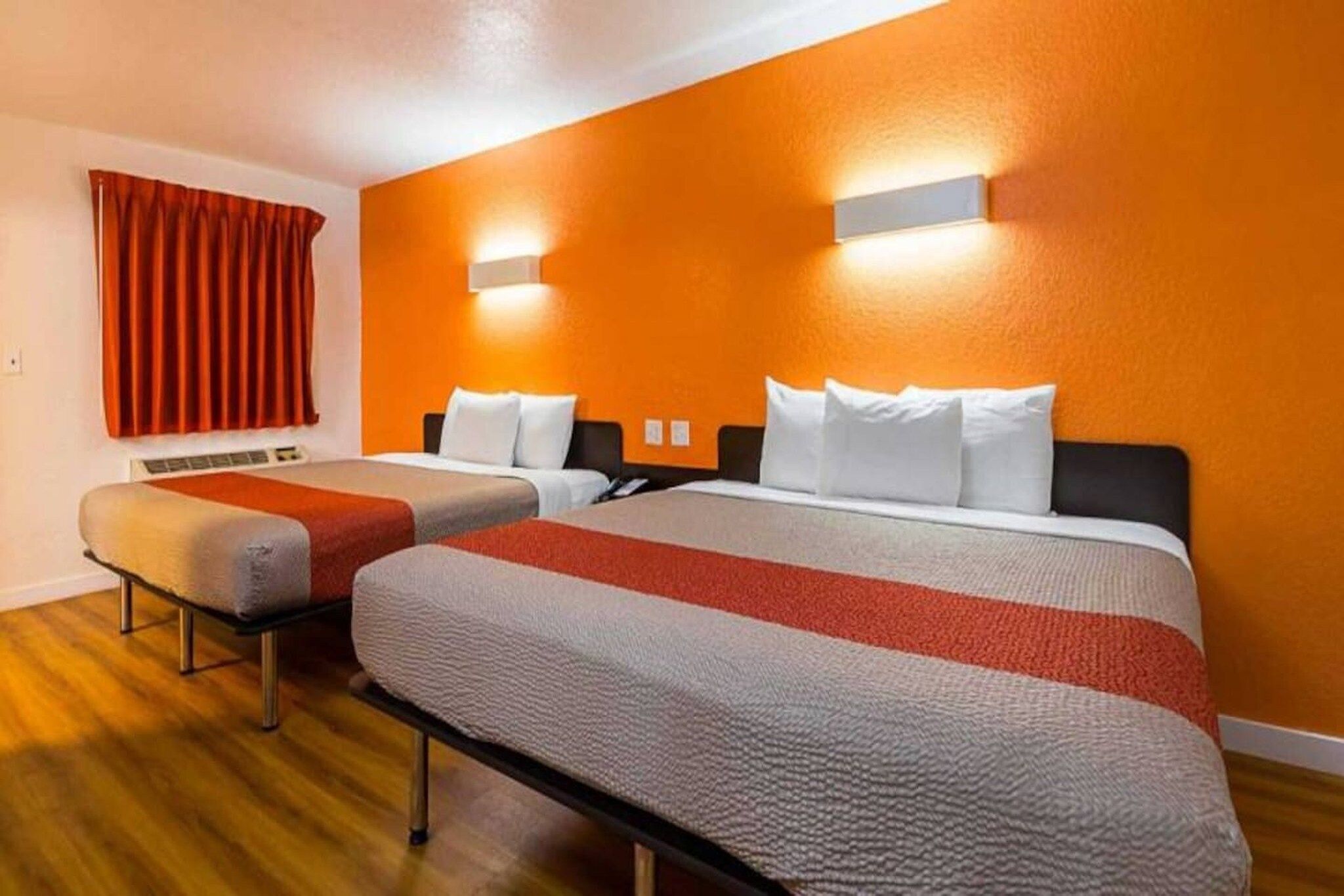 A hotel room with two beds, a red curtain, and a wooden floor.