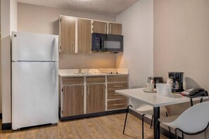A compact kitchenette with a refrigerator, microwave, and wooden cabinets. There is a small dining table with chairs, a coffee maker, and a telephone. - 2 Queen Beds | Smoking, Kitchen (Dallas)