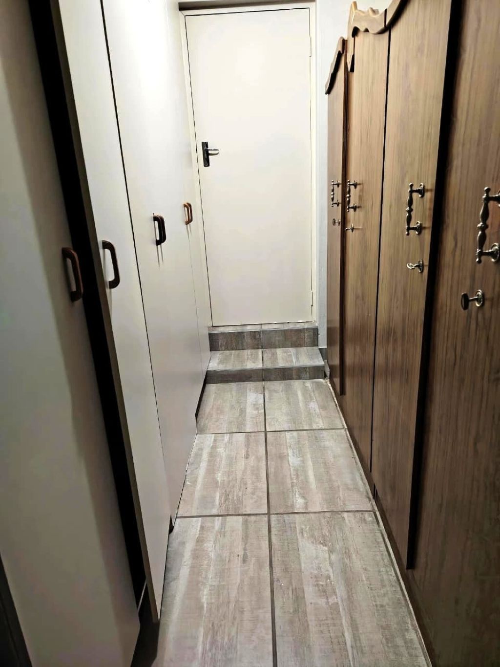 A narrow hallway with a wooden floor, white walls, and a door at the end.