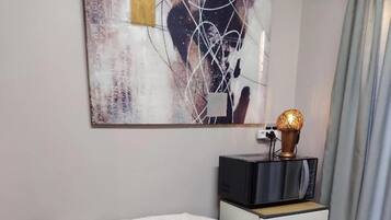 Une pièce confortable avec un canapé moelleux, une petite table d’appoint en bois, une lampe décorative et un téléviseur fixé au mur.