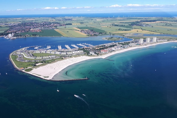 An aerial view of a coastal resort with a marina, sandy beach, and a curved bay. - Studio im IFA Fehmarn Ferienpark (Fehmarn)