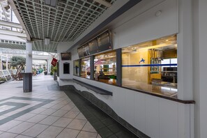 A commercial area with a restaurant featuring a blue logo, a tiled floor, and a covered walkway. - Studio im IFA Fehmarn Ferienpark (Fehmarn)