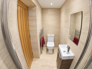 Un baño moderno con puerta de madera, inodoro blanco, lavamanos con espejo y toalla roja.