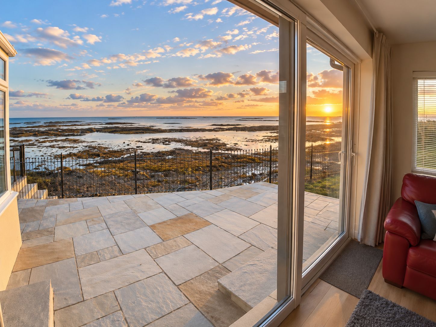 A balcony with a view of the sea and sunset, a red leather sofa, and a glass door leading to the balcony.