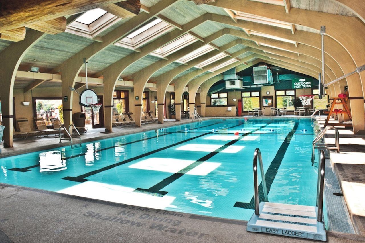 An indoor swimming pool with multiple lanes, a basketball hoop, and a sign for outdoor hot tubs.