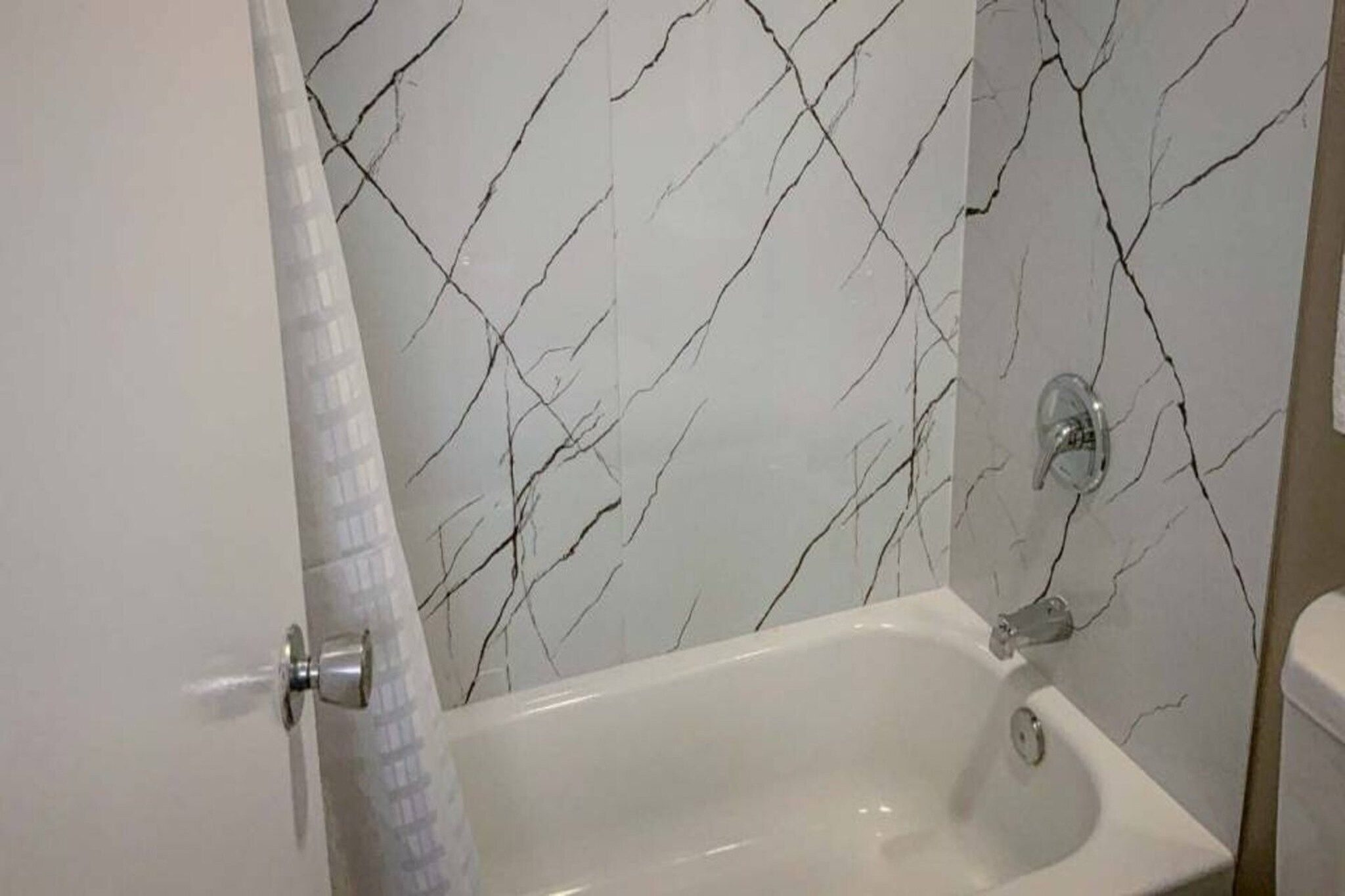 Une salle de bain avec une baignoire blanche, un rideau de douche et un mur décoré d’un motif imitant le marbre.