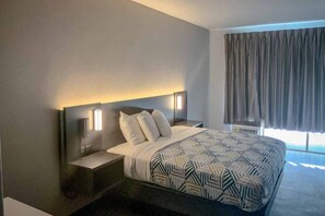 A modern hotel room with a large bed, two bedside tables, a nightstand, and a window with curtains. - 1 King Bed | Non-Smoking, Kitchen (San Angelo)