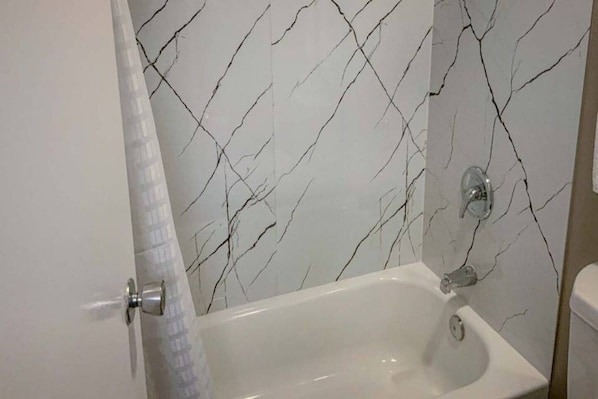 Un baño con una bañera blanca, cortina de ducha y pared con estampado de mármol.