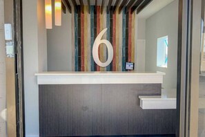 A reception desk with a large number '6' on the wall, a modern design with a grey countertop, and a vertical striped pattern behind the number. - 2 Full Beds | Smoking, Kitchen (San Angelo)