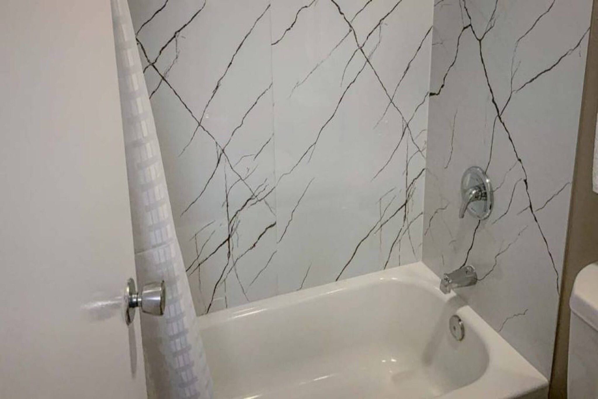 Une salle de bain avec une baignoire blanche, un rideau de douche et un mur décoré d’un motif imitant le marbre.