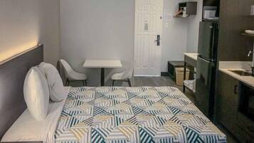 A hotel room with a bed, two chairs, a small table, a refrigerator, and a door.