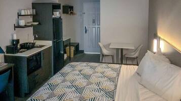 Ein kleines Hotelzimmer mit Bett, einer kleinen Küchenzeile, einem Esstisch mit Stühlen und einer Tür zu einem weiteren Raum.