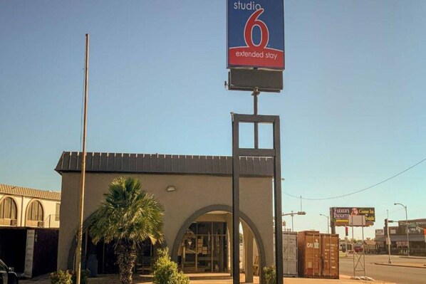 Hotel amb un cartell destacat que diu '6 extended stay', una entrada gran d'arc i una palmera al primer pla.