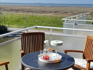 Ein Balkon mit rundem Tisch, zwei Stühlen, einer Ablage mit Gläsern und einer Flasche sowie Blick auf den Ozean.