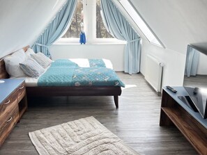 Ein Schlafzimmer mit einem Bett, einem Schminktisch, einem Fernseher und einem Fenster mit Vorhängen.