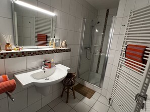 Ein Badezimmer mit einem weißen Waschbecken, einer Duschkabine aus Glas und einem Handtuchhalter mit Handtuch.