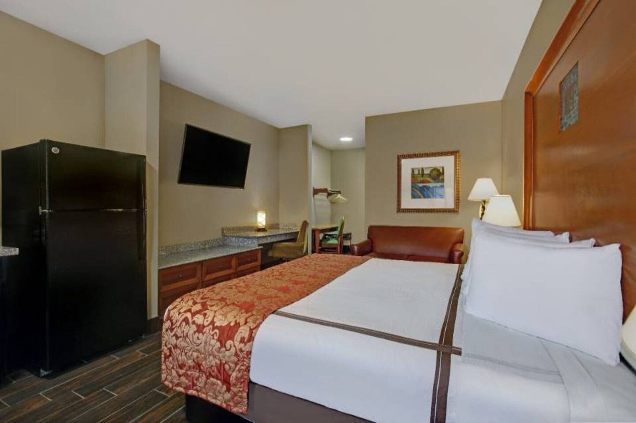 A hotel room with a bed, a desk, a refrigerator, and a television on the wall.