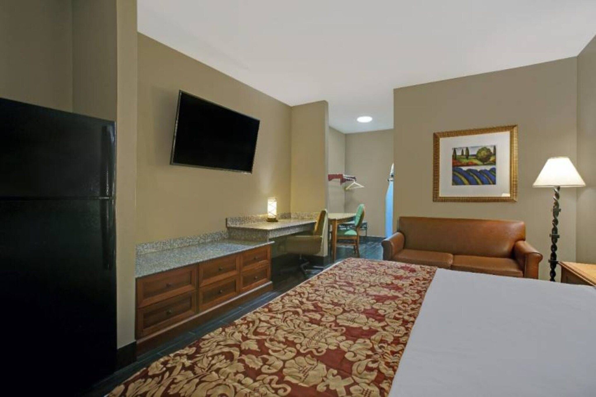 Una habitación de hotel con cama, escritorio, silla, televisión y un cuadro en la pared.