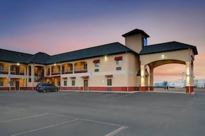 Et motel med flere balkoner, en parkeringsplads og en stor buegangsindgang.