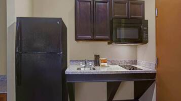 A compact kitchen with a black refrigerator, a microwave, and a granite countertop.