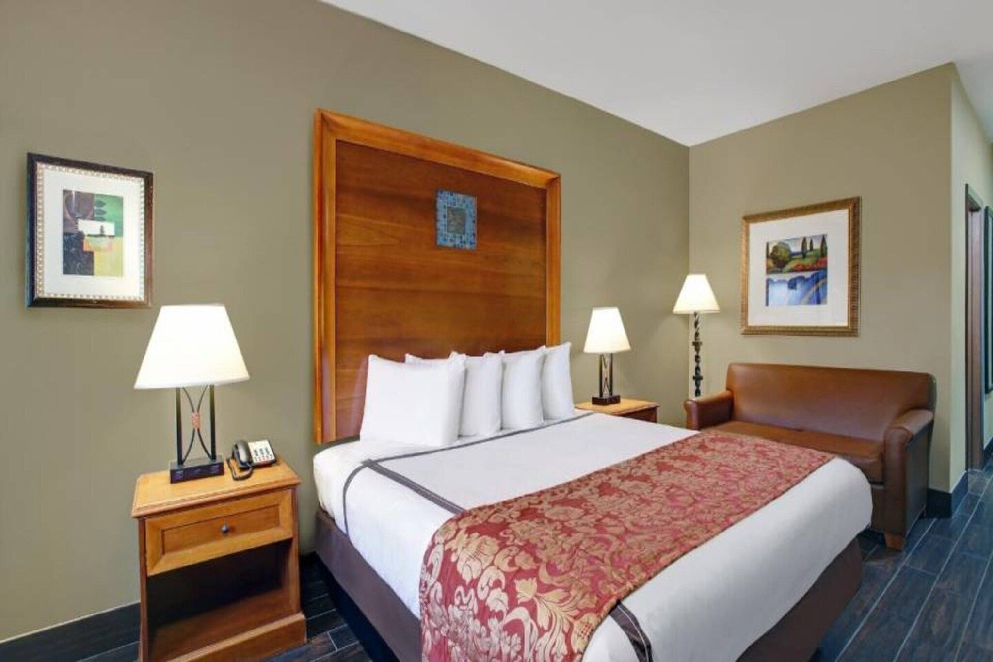 Een hotelkamer met een groot bed, twee nachtkastjes met lampen, een houten hoofdbord en twee ingelijste foto's aan de muur.