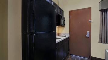 Cocina compacta con refrigerador negro, microondas y puerta marrón.